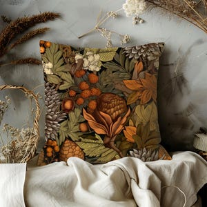 May include: Square throw pillow with a botanical design featuring a variety of leaves, berries, and pinecones in shades of green, brown, orange, and cream. The pillow has a dark background and a detailed, artistic pattern.
