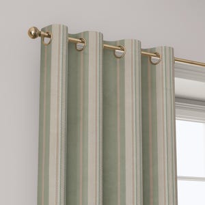 May include: A sage green curtain panel featuring vertical stripes in white and thin tan lines. The fabric is suspended from a gold-toned metal rod by integrated circular grommets, creating uniform folds along the length of the window covering.