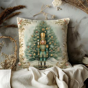 May include: A decorative throw pillow with a vintage illustration of a nutcracker standing in front of a Christmas tree. The pillow features a cream background with gold accents and a green Christmas tree.