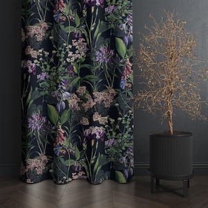 May include: Dark floral curtain with a botanical print featuring purple, pink, and green flowers on a black background. The curtain is next to a black planter with a dried plant.