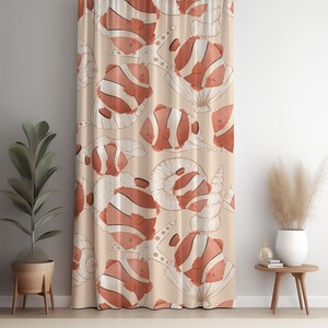 May include: A beige curtain with a repeating pattern of cartoon clownfish in orange and white stripes, along with white seashell and starfish outlines. The curtain is hanging in front of a wall, with a potted plant and side table visible.