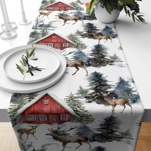 May include: A white table runner with a winter wonderland theme. The runner features red houses, green trees, and brown deer. The design is painted in a watercolor style.