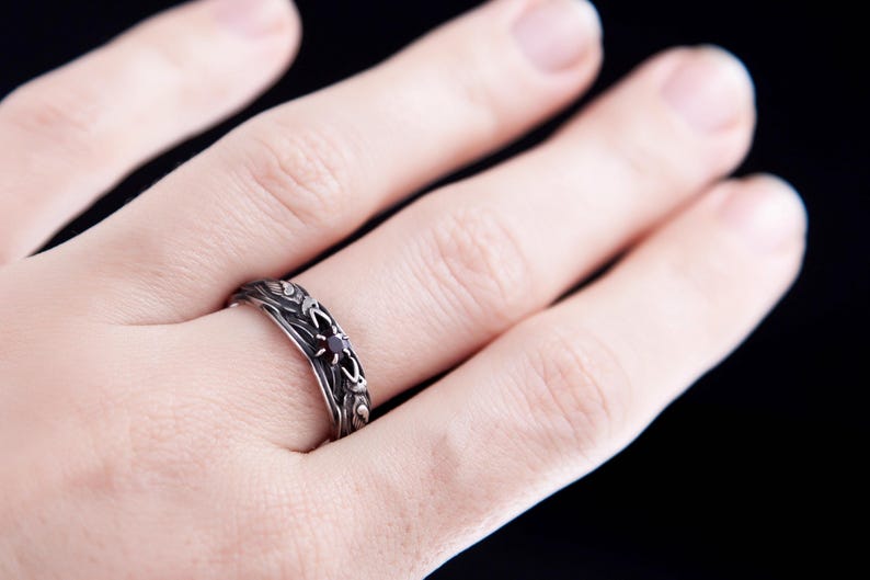 Sterling silver Viking ring featuring Odin's ravens Huginn and Muninn, holding a 3mm natural garnet. Handmade Norse mythology jewelry