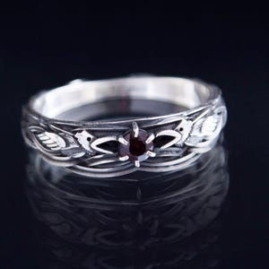 Sterling silver Viking ring featuring Odin's ravens Huginn and Muninn, holding a 3mm natural garnet. Handmade Norse mythology jewelry