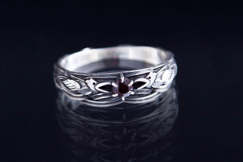 Sterling silver Viking ring featuring Odin's ravens Huginn and Muninn, holding a 3mm natural garnet. Handmade Norse mythology jewelry