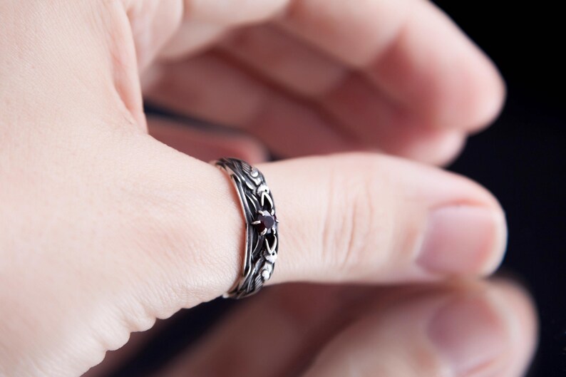 Sterling silver Viking ring featuring Odin's ravens Huginn and Muninn, holding a 3mm natural garnet. Handmade Norse mythology jewelry