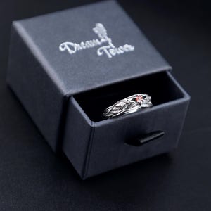 Gothic raven ring with garnet nestled in a black Dream Tower branded gift box, lid open at an angle on a dark background