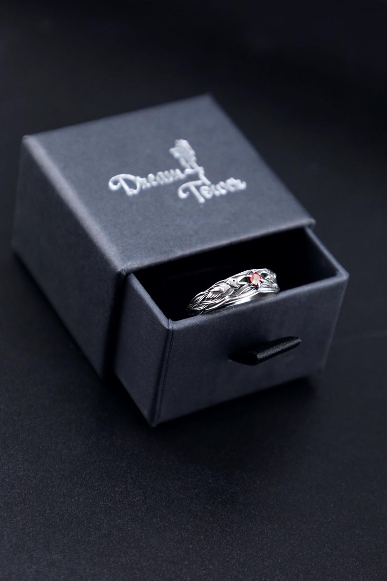 Gothic raven ring with garnet nestled in a black Dream Tower branded gift box, lid open at an angle on a dark background