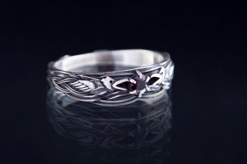 Sterling silver Viking ring featuring Odin's ravens Huginn and Muninn, holding a 3mm natural garnet. Handmade Norse mythology jewelry