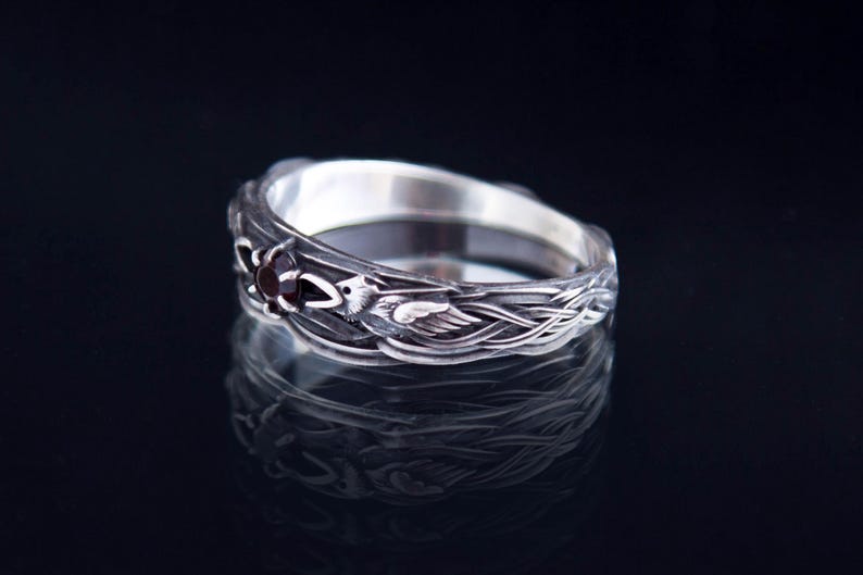 Sterling silver Viking ring featuring Odin's ravens Huginn and Muninn, holding a 3mm natural garnet. Handmade Norse mythology jewelry