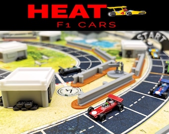 May include: A board game with a race track and miniature cars. The game is called "HEAT F1 CARS". The cars are red, blue, and green. There are also small buildings and a start line.
