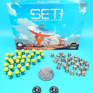 Peut inclure: Une boîte de jeu de société intitulée "SETI" avec le texte "Recherche d'intelligence extraterrestre". Le jeu comprend des dés, des jetons et des piles miniatures. L'illustration de la boîte représente des radiotélescopes sous un ciel bleu.