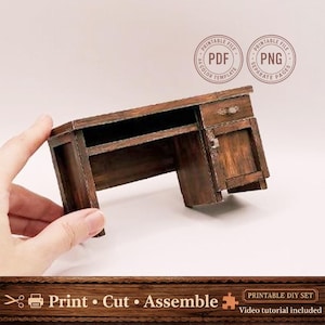 Op de afbeelding: Een kleine, donkerbruine houten bureau met een lade, een kastdeur en een plank. Het bureau maakt deel uit van een printbare doe-het-zelf set, zoals aangegeven door de tekst en de ronde logo's. De tekst "Print Cut Assemble" is ook zichtbaar.