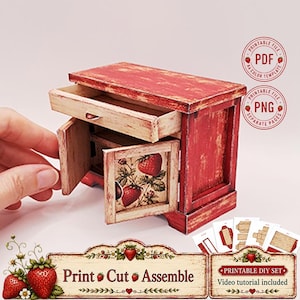Puede incluir: Un armario de madera en miniatura con acabado desgastado en rojo y crema, que cuenta con un cajón y dos puertas decoradas con ilustraciones de fresas. El set incluye plantillas PDF y PNG imprimibles, etiquetadas como Print Cut Assemble.