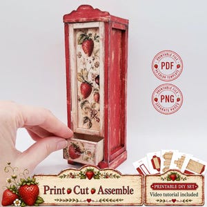 Può includere: Un armadietto in legno in miniatura con una finitura rossa anticata e una stampa botanica di fragole sul pannello frontale. L'armadietto è dotato di un piccolo cassetto estraibile. Sono inclusi file PDF e PNG stampabili per un progetto fai-da-te.