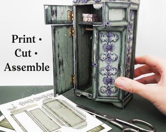 May include: A miniature, open-door wardrobe with a distressed green finish and purple floral accents. The text "Print • Cut • Assemble" is visible. The wardrobe is next to cut-out paper pieces and scissors.