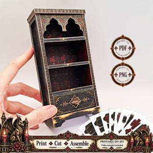 May include: A miniature black wooden-style cabinet with two shelves and a bottom drawer, featuring gothic-inspired arches and floral interior patterns. Includes printable PDF and PNG templates for assembly, labelled Print, Cut, Assemble.