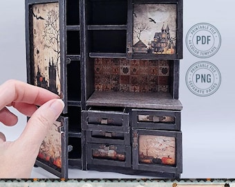 May include: A miniature black cabinet with drawers and shelves, featuring Halloween-themed artwork. The cabinet has a distressed finish and includes images of a haunted house, trees, and pumpkins. The text "Print Cut Assemble" is visible.