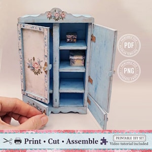 May include: A miniature blue cabinet with open doors, shelves, and floral accents. The cabinet has a distressed finish and includes small decorative boxes inside. The text "Print Cut Assemble" is visible at the bottom.