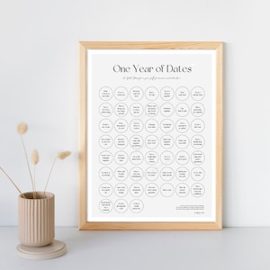 May include: A printable poster with a white background and black text. The poster is framed in a light wood frame. The poster has the title "One Year of Dates" and lists 52 date ideas in circles.