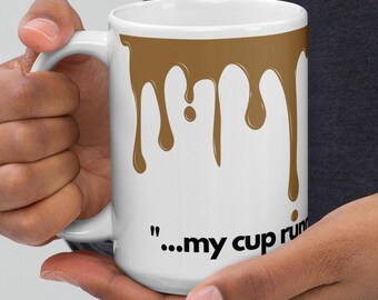 May include: White ceramic mug with a brown, dripped paint design. The mug features the phrase "...my cup run" in black text. The mug is held by a person.