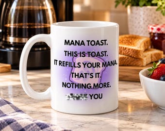 May include: A white ceramic mug featuring a purple gradient background and a graphic of a piece of toast. The text reads: MANA TOAST. THIS IS TOAST. IT REFILLS YOUR MANA. THAT'S IT. NOTHING MORE. [BLURRED TEXT] YOU.