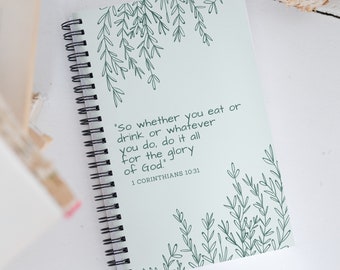 May include: A green spiral bound journal with a quote from the Bible, "So whether you eat or drink or whatever you do, do it all for the glory of God." 1 Corinthians 10:31, and a leafy design.
