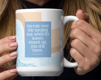 May include: White ceramic mug with a handle, featuring a blue square with the text "You rule over the surging sea; when its waves mount up, you still them. Psalm 89:9." The mug has a light blue and beige design.