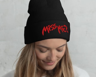 May include: A black cuffed beanie featuring the text MISS ME? embroidered in bright red thread across the front. The knit hat has a ribbed texture and a folded brim, providing a simple and bold look with clear, legible red lettering.