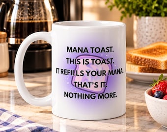 May include: A white ceramic mug featuring a purple gradient background with a graphic of a slice of toast. The text reads: MANA TOAST. THIS IS TOAST. IT REFILLS YOUR MANA. THAT'S IT. NOTHING MORE. The mug has a handle on the left side.