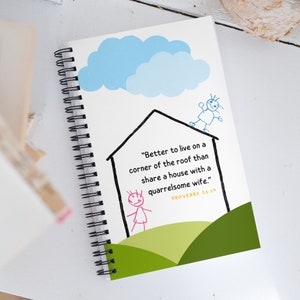 May include: A spiral bound notebook with a white cover featuring a cartoon illustration of a house with a person on the roof and another person standing in the yard. The text on the cover reads "Better to live on a corner of the roof than share a house with a quarrelsome wife."  PROVERBS 21:19