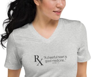 May include: Light gray v-neck t-shirt with the text "A cheerful heart is good medicine..." and the Rx symbol. The text is in black, with the reference "Proverbs 17:22" below the quote. The shirt is a soft, comfortable material.