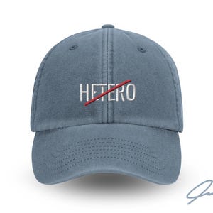 Könnte beinhalten: Eine blaue Denim-Baseballkappe mit dem Wort "HETERO" in Weiß gestickt, durchgestrichen mit einem roten Strich. Die Kappe hat einen gebogenen Schirm und einen verstellbaren Riemen.