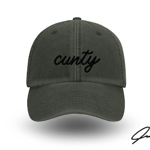 Könnte beinhalten: Dunkelgrüne Baseballkappe mit dem Wort "c**ty" in schwarzer Schrift auf der Vorderseite. Die Kappe hat einen gebogenen Schirm und ein genähtes Design. Eine Signatur befindet sich in der unteren rechten Ecke.