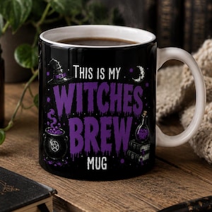May include: A black ceramic mug with a white interior and handle. The front features purple text that reads This is my WITCHES BREW MUG, accompanied by illustrations of a witch hat, a crescent moon, a bubbling cauldron, and a potion bottle.