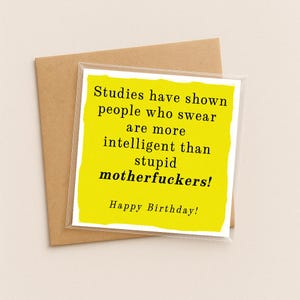 May include: A square greeting card with a bright yellow front featuring black text that reads: Studies have shown people who swear are more intelligent than stupid motherfuckers! Happy Birthday! The card is placed against a brown envelope.