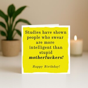 May include: A square greeting card with a bright yellow background and black text that reads: Studies have shown people who swear are more intelligent than stupid motherfuckers! Happy Birthday! The card has a textured, painted-style border.