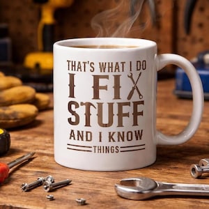 May include: White coffee mug with the text "THAT'S WHAT I DO I FIX STUFF AND I KNOW THINGS" in brown lettering. The mug is filled with coffee, and steam rises from the top. Tools and hardware are scattered on a wooden surface.