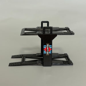 Puede incluir: Soporte de elevaci&oacute;n de coche de pl&aacute;stico negro con un logotipo de Martini Racing. El soporte tiene dos rampas y una plataforma.