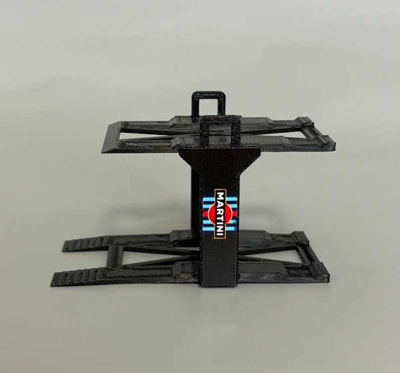 Puede incluir: Soporte de elevaci&oacute;n de coche de pl&aacute;stico negro con un logotipo de Martini Racing. El soporte tiene dos rampas y una plataforma.