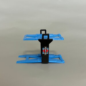 Puede incluir: Un elevador de coches de pl&aacute;stico negro y azul con un logotipo de Martini Racing. El elevador est&aacute; dise&ntilde;ado para sujetar coches de juguete.