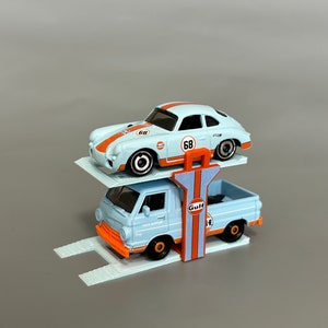 Puede incluir: Un transportador de coches de juguete azul con un coche de juguete blanco en la parte superior. El transportador tiene un logotipo de Gulf y el coche tiene el n&uacute;mero 68.