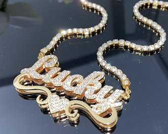 May include: A gold necklace with the word "Lucky" in a cursive font, embellished with small, sparkling stones. The necklace has a delicate chain of similar stones, creating a glamorous accessory.