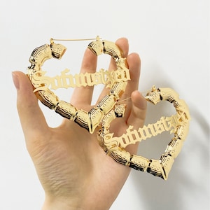 May include: A pair of gold-tone heart-shaped hoop earrings with the word "Sophisticated" written in a gothic font.