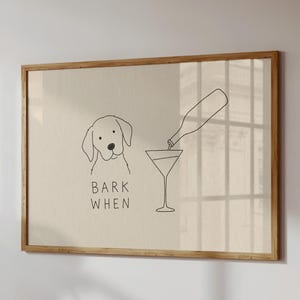 K&ouml;nnte beinhalten: Ein gerahmter Kunstdruck mit einer minimalistischen schwarzen Strichzeichnung auf beigem Hintergrund. Die Abbildung zeigt einen Hund neben einem Martiniglas, das aus einer Flasche gef&uuml;llt wird, mit dem Text BARK WHEN unter dem Kopf.