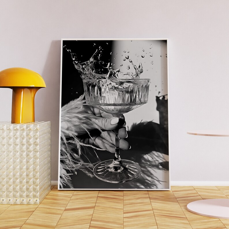 May include: A black and white photograph of a hand holding a stemmed glass with water splashing out of it.