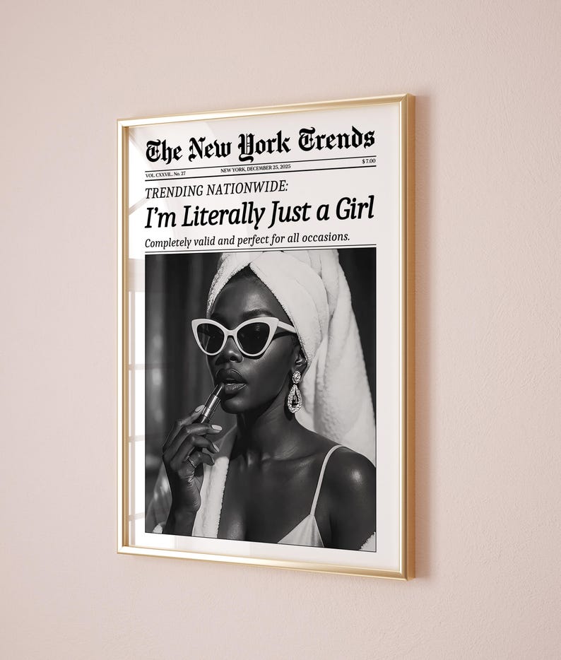 May include: A framed black and white print featuring a woman applying lipstick, wearing white sunglasses, and a towel on her head. The print is a mock newspaper with the headline "I'm Literally Just a Girl."