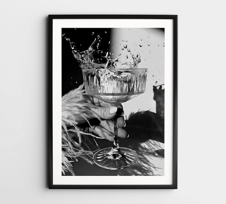 May include: A black and white photograph of a hand holding a crystal glass with water splashing out of it.