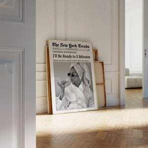 K&ouml;nnte beinhalten: Ein gerahmter Schwarz-Wei&szlig;-Druck einer Frau im Bademantel und Sonnenbrille, die ein Glas h&auml;lt. Der Druck tr&auml;gt den Titel "The New York Trends" mit der &Uuml;berschrift "I'll Be Ready in 5 Minutes."