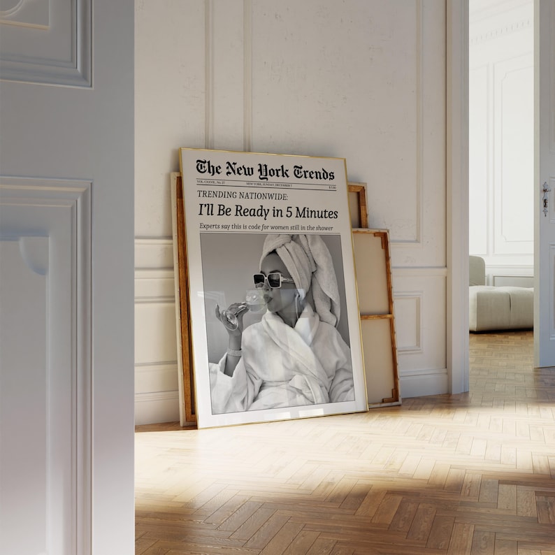 K&ouml;nnte beinhalten: Ein gerahmter Schwarz-Wei&szlig;-Druck einer Frau im Bademantel und Sonnenbrille, die ein Glas h&auml;lt. Der Druck tr&auml;gt den Titel "The New York Trends" mit der &Uuml;berschrift "I'll Be Ready in 5 Minutes."